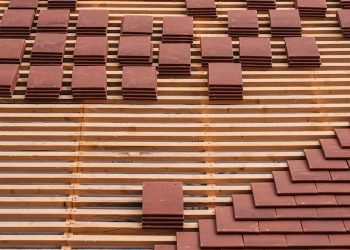 Close-up of red clay tiles being placed on a roof, showcasing construction and craftsmanship.