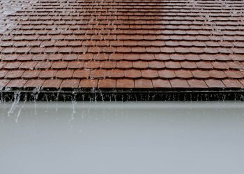 Brown roof tiles with rainwater cascading down, showcasing architectural texture and detail.