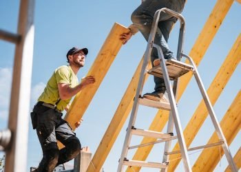 Two construction workers building a wooden roof structure on a sunny day.